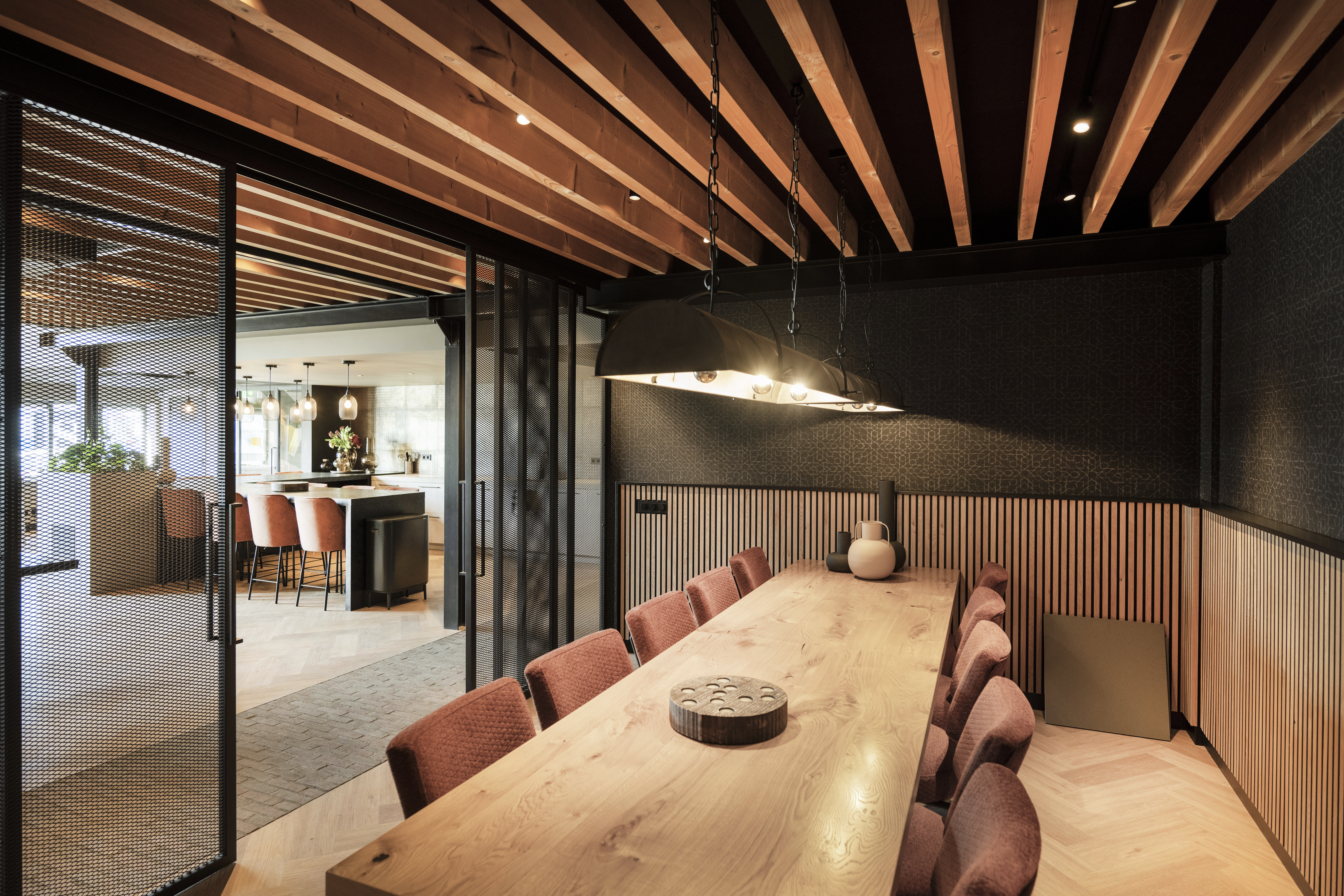 Interieur van een stoere vergaderruimte bij de Van der Werff Groep, gekenmerkt door een open houten balkenplafond met spotjes, roze stoelen, akoestische wanden en zwarte gaaswanden.